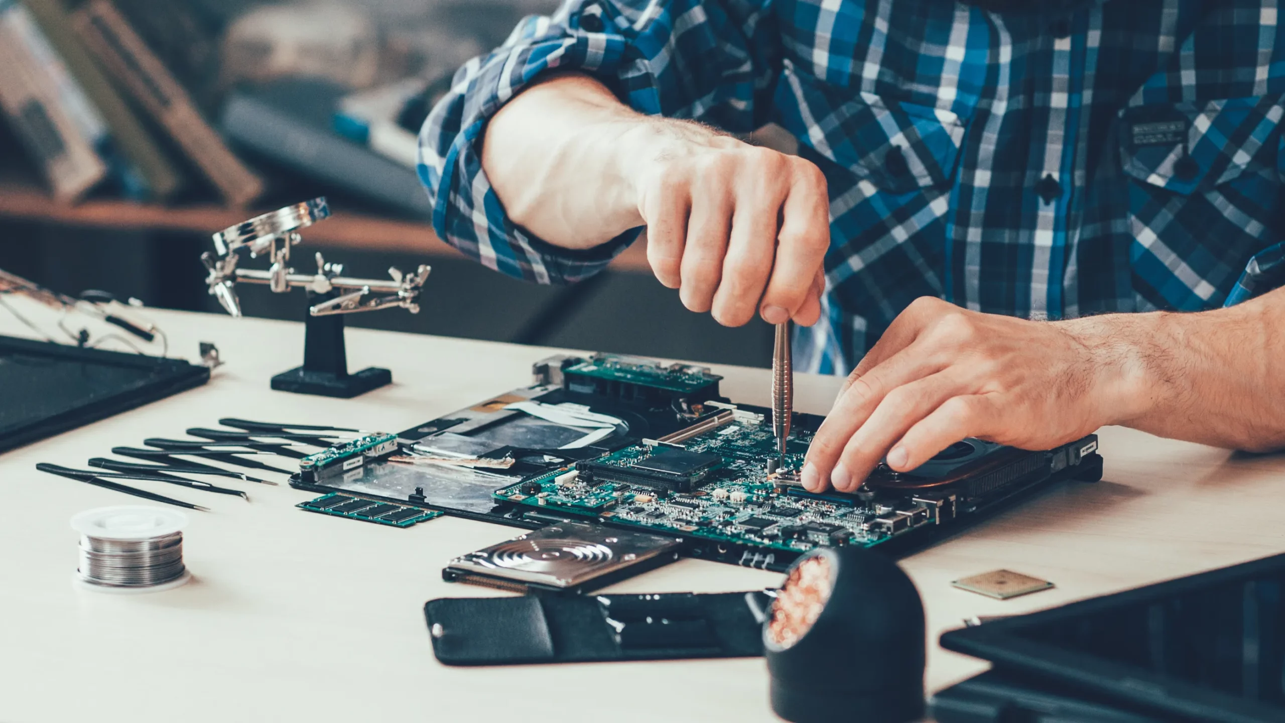 Noggrann elektronikreparation på komponentnivå Person reparerar en moderkortsenhet med specialverktyg på ett arbetsbord.